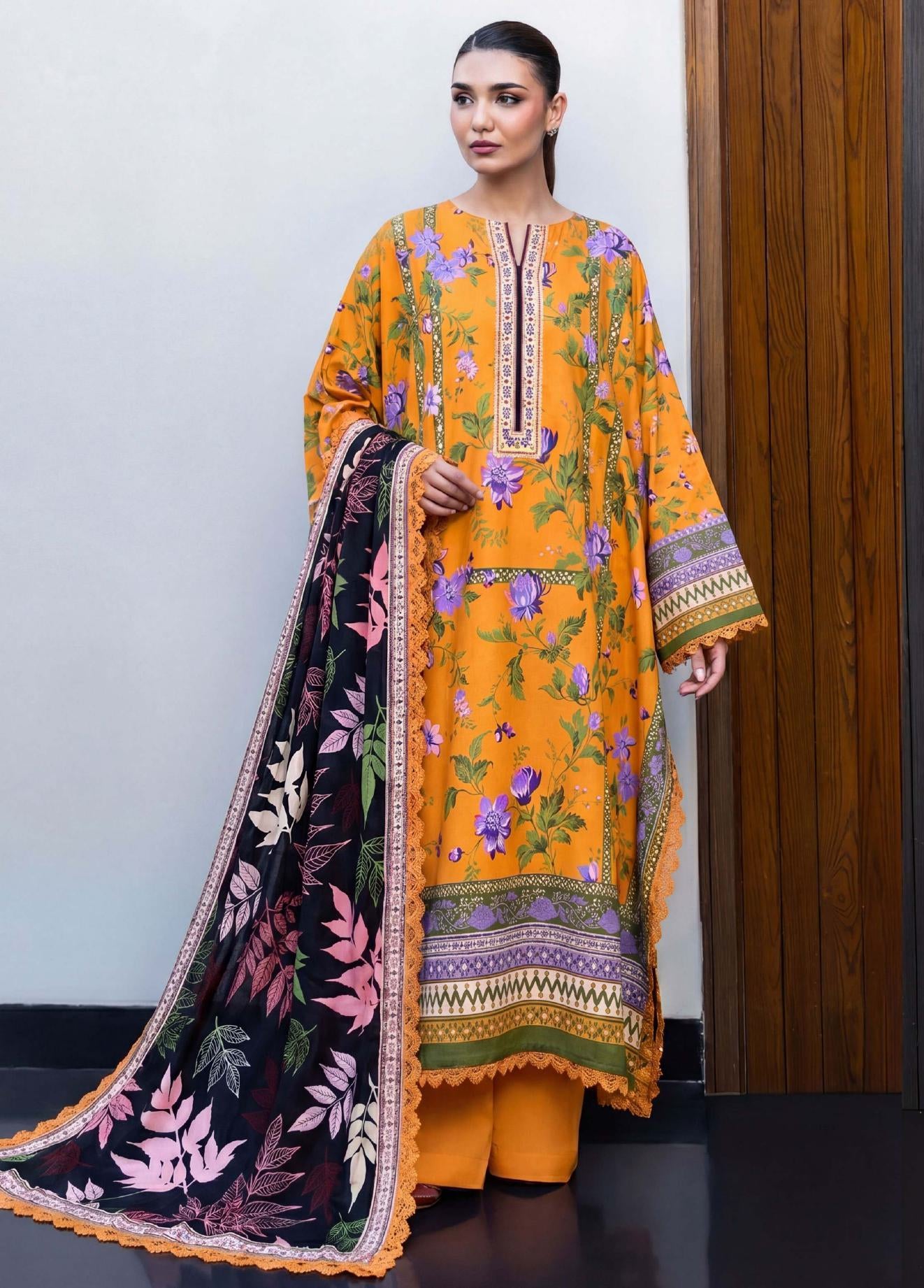 Woman wearing a mustard yellow floral dress with a dark floral dupatta in a minimal indoor setting.