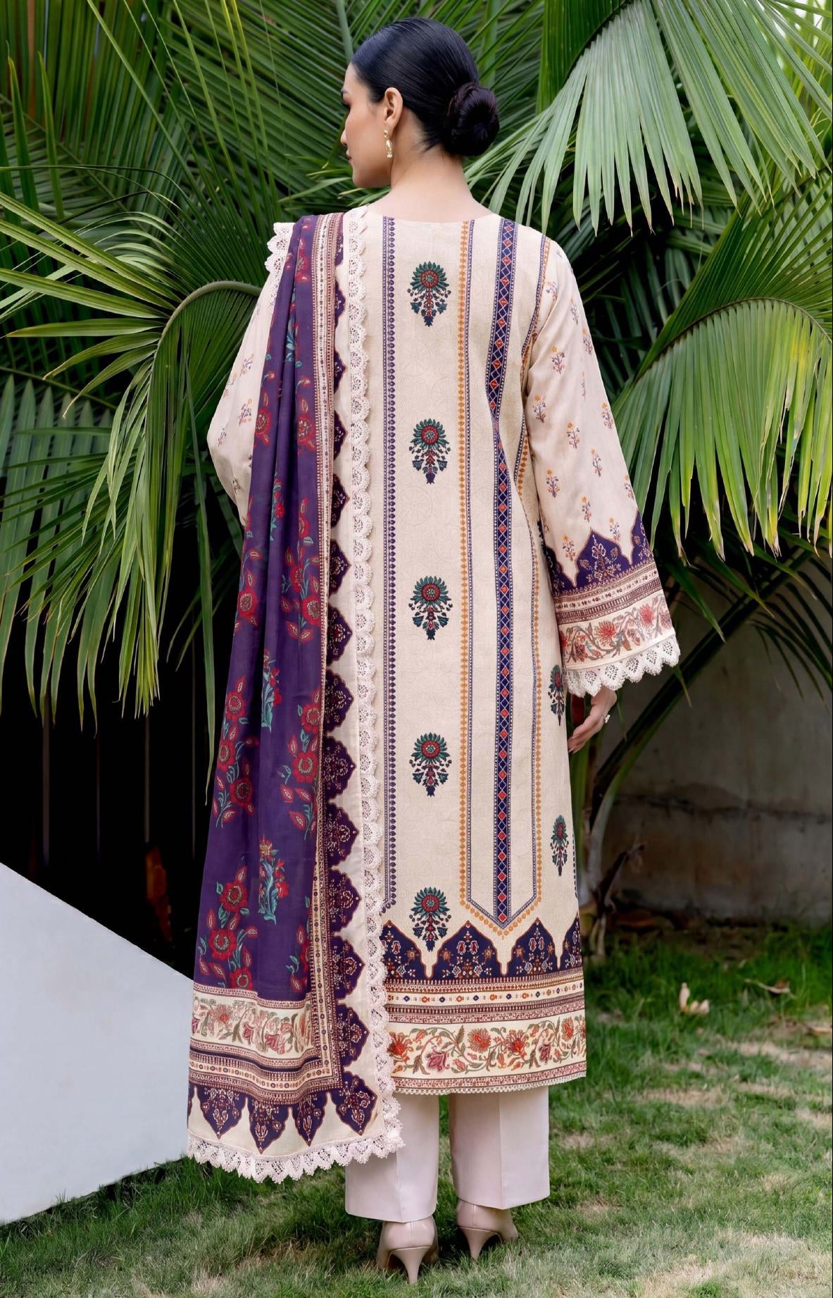 Woman wearing a traditional outfit with intricate patterns in front of green foliage.